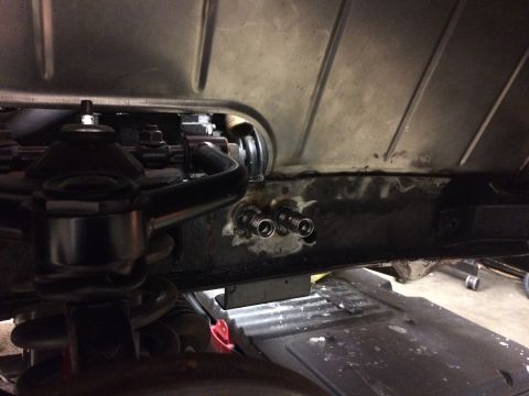 1964 Ford Fairlane - A close-up view of the underside of a vehicle, showing suspension components and two metal fittings welded to a frame rail.