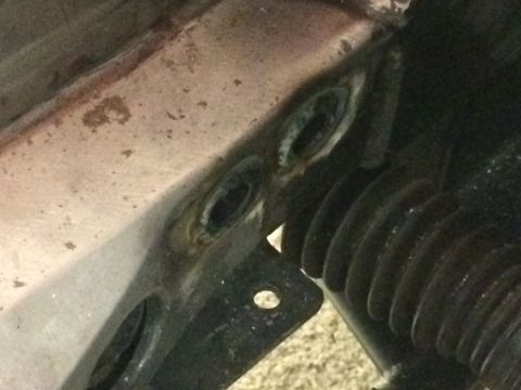 1964 Ford Fairlane - Close-up view of rusted mounting holes on a vehicle's frame rail, with a black rubber bellows visible to the right.