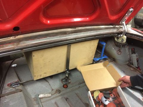 1964 Ford Fairlane - The open trunk of a red 1964 Ford Fairlane shows a custom wooden enclosure mounted inside, possibly for audio equipment. A box of sanding d…