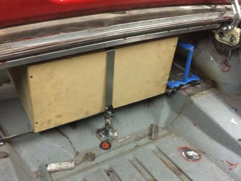 1964 Ford Fairlane - A custom wooden box is mounted under the rear deck of a classic car, secured with metal straps and brackets. The car's trunk floor is visib…
