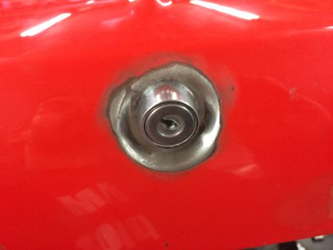 1964 Ford Fairlane - A close-up view of a keyhole lock cylinder installed in a red car body panel. The lock cylinder is silver and has a visible keyhole with a…