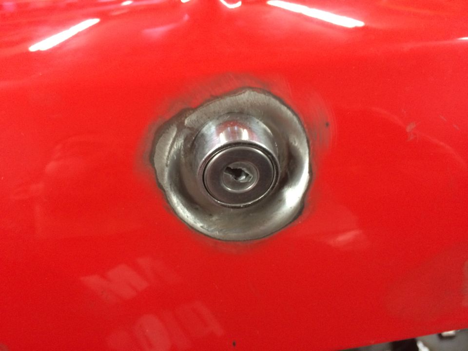 Close-up of a silver keyhole lock cylinder on a red car body panel.