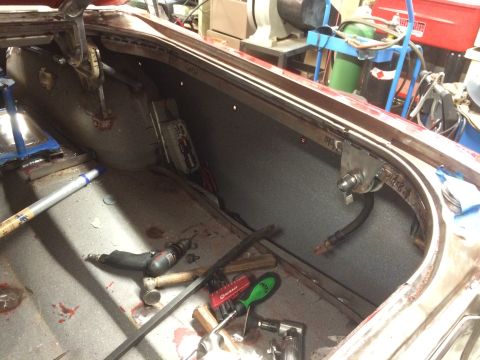 1964 Ford Fairlane - The interior of a classic car trunk is shown, with various tools and parts laid out. A metal bracket with a bolt and hose is mounted to the…