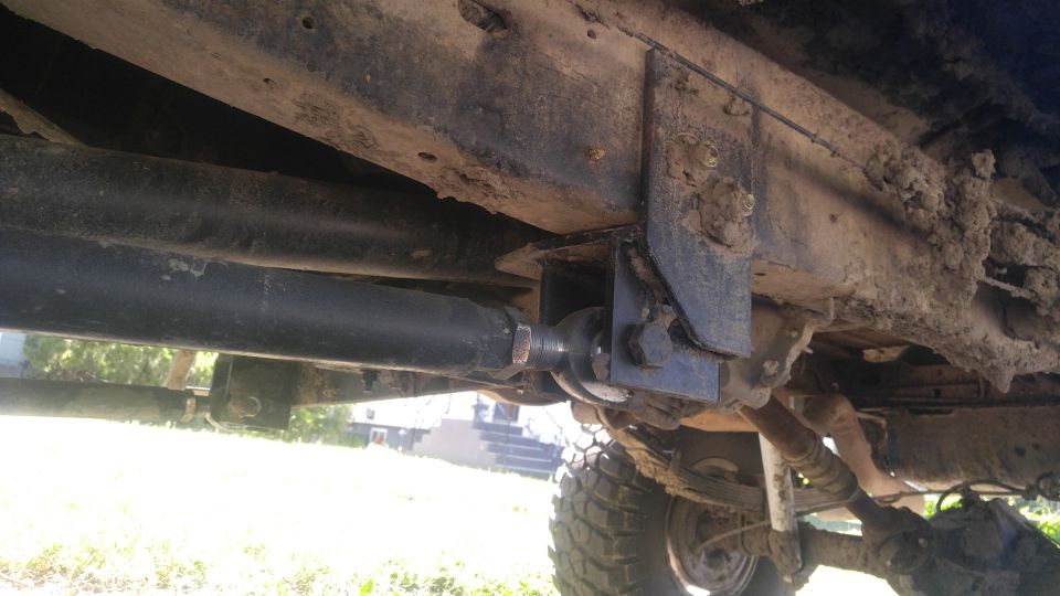 Underside of a vehicle showing modified suspension, frame, and steering components covered in mud.