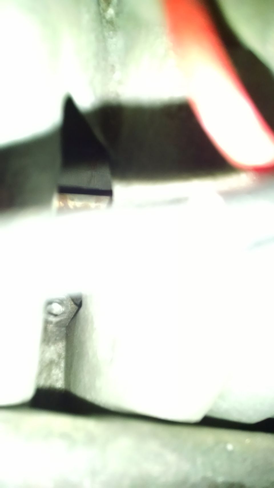 Close-up of a metallic component with a sharp edge, blurry background with red object.