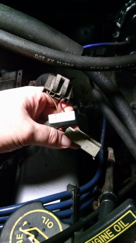 1995 Ford Bronco - A hand holds two disconnected electrical connectors in an engine bay. One connector is gray and rectangular with multiple pins, while the o…