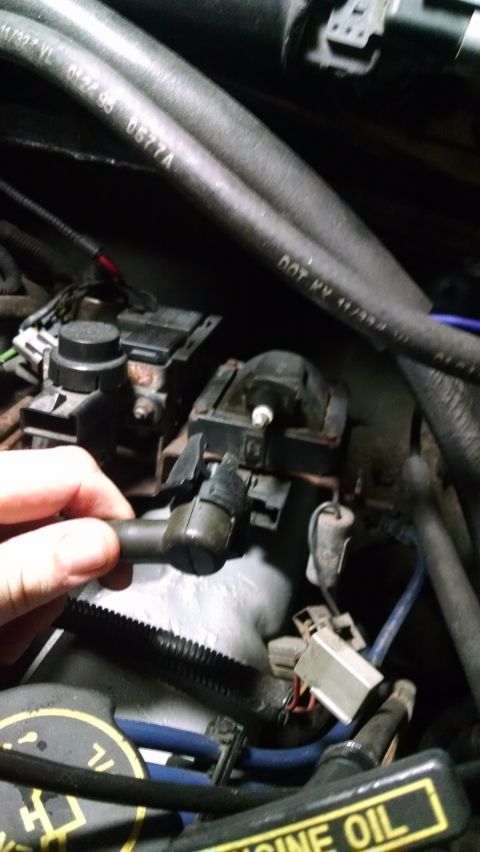 1995 Ford Bronco - A close-up view of a person's hand holding a spark plug wire disconnected from a Ford Bronco engine. Various engine components, hoses, and…