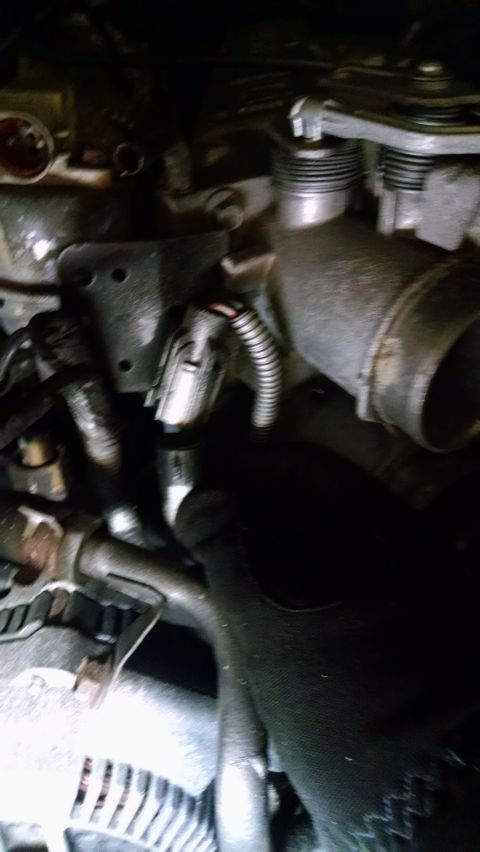 1995 Ford Bronco - This is a close-up view of engine components in a dimly lit area. A gray electrical connector with a ribbed hose attached is visible, along…