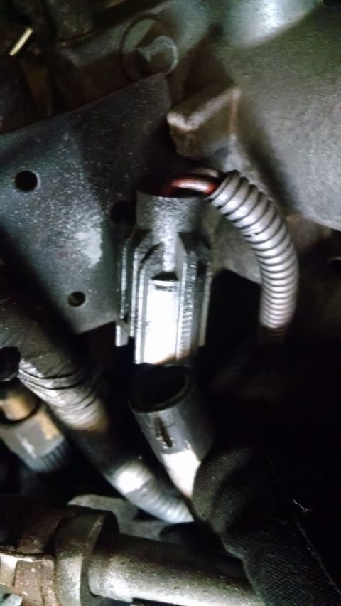 1995 Ford Bronco - A close-up view of a silver electrical connector with red wires attached, situated within an engine bay. The connector is partially obscure…