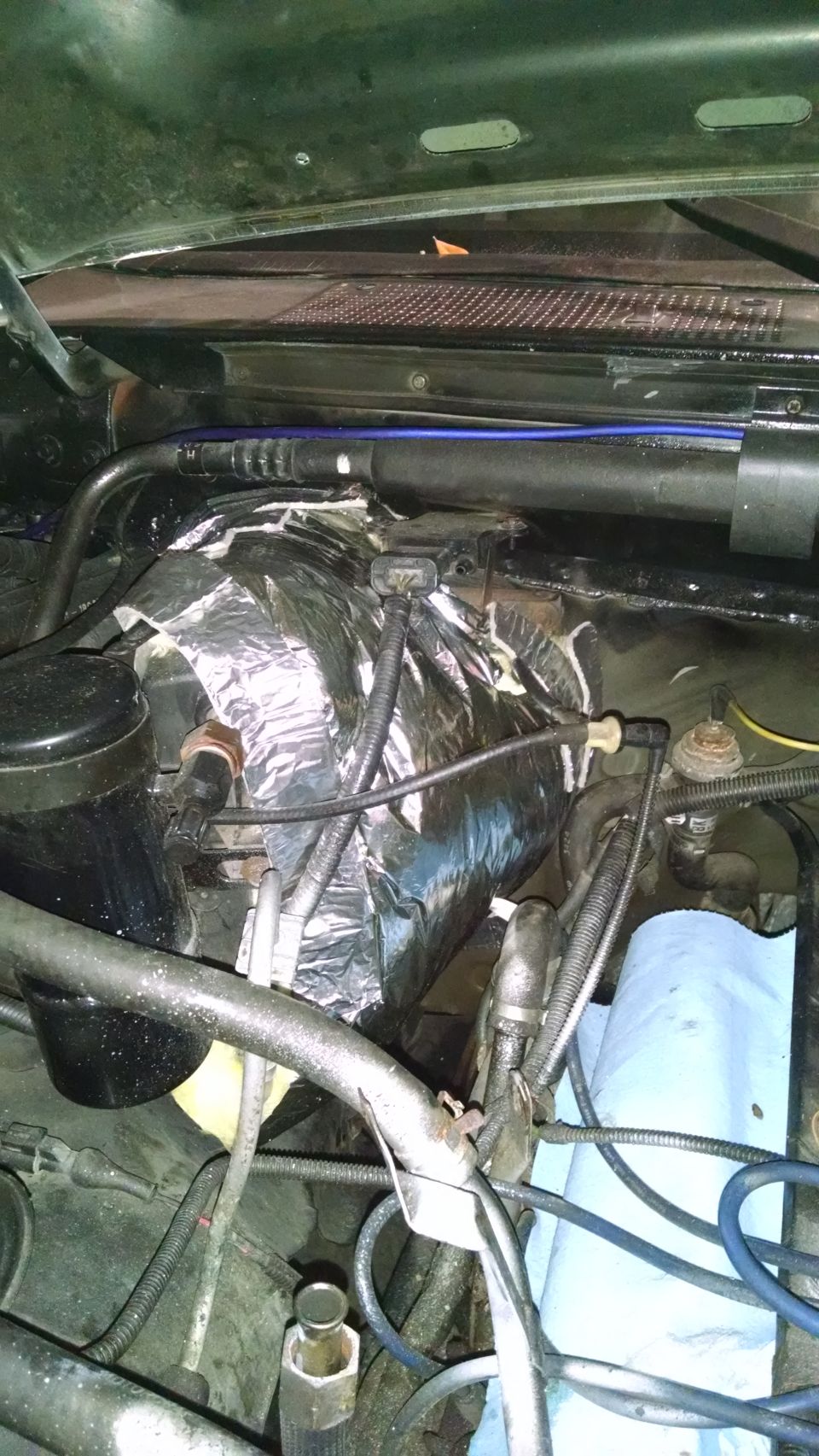 Engine bay of a 1995 Ford Bronco with hoses, wiring, and reflective insulation.