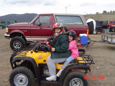 1996 Ford Bronco - A woman and a young girl wearing helmets ride on a yellow ATV, with a red Ford Bronco parked behind them. A trailer is attached to the Bron…
