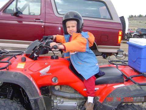 1996 Ford Bronco - A young boy wearing a helmet and riding gear sits on a red Honda ATV in front of a dark red Ford Bronco. A blue cooler is mounted on the re…