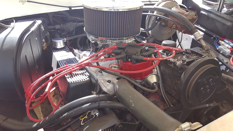 Engine bay of a classic vehicle with chrome air cleaner, red spark plug wires, and distributor cap.