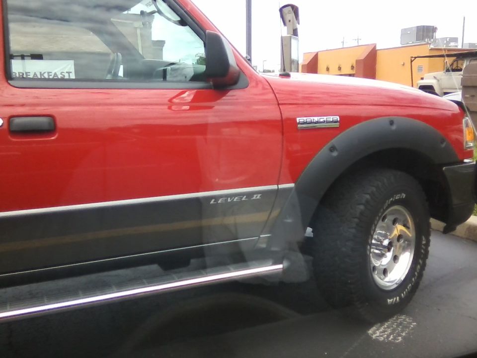Red Ford Ranger pickup truck, right side view, with "BREAKFAST" sticker on window.