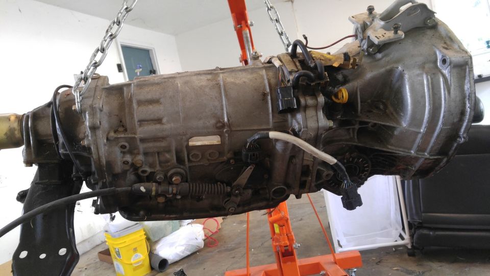 Gray Subaru Legacy automatic transmission hanging from an engine hoist.