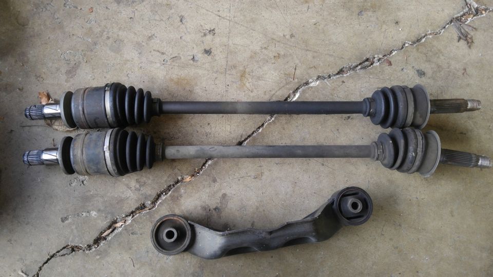 Two CV axles and a control arm on a concrete surface.