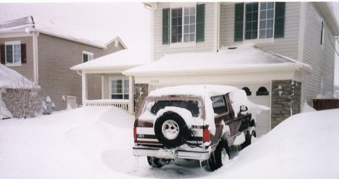1996 Ford Bronco - A maroon Ford Bronco is heavily covered in snow, parked in a driveway during a blizzard. The vehicle is almost completely buried, with only…