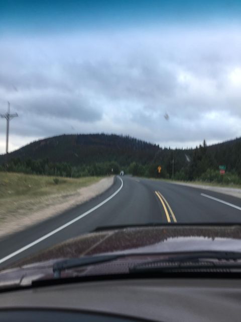 1996 Ford Bronco - The interior of a vehicle is shown, looking out through the windshield at a highway curving through a forested, hilly landscape under a clo…