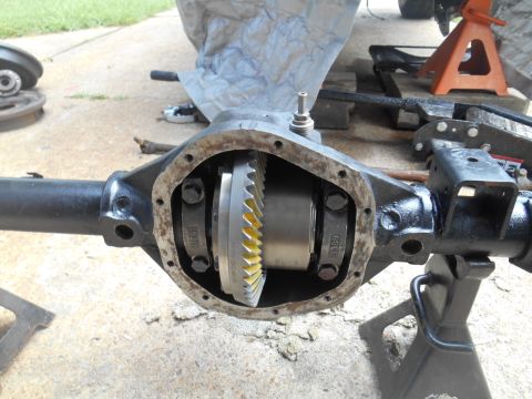 1972 Ford Bronco - A close-up view of an open differential housing with gears visible. The housing is black and supported by jack stands on a concrete surface.