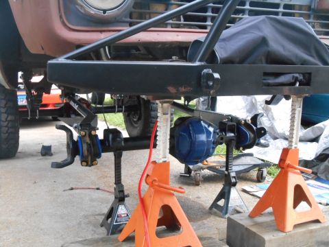 1972 Ford Bronco - A custom front axle assembly, painted blue, is mounted on jack stands beneath a vehicle frame. The vehicle appears to be a Ford Bronco, wit…