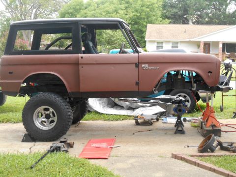 1972 Ford Bronco - A 1972 Ford Bronco is shown in a side profile, lifted on jack stands with its wheels removed. The vehicle is in a state of repair or modifi…