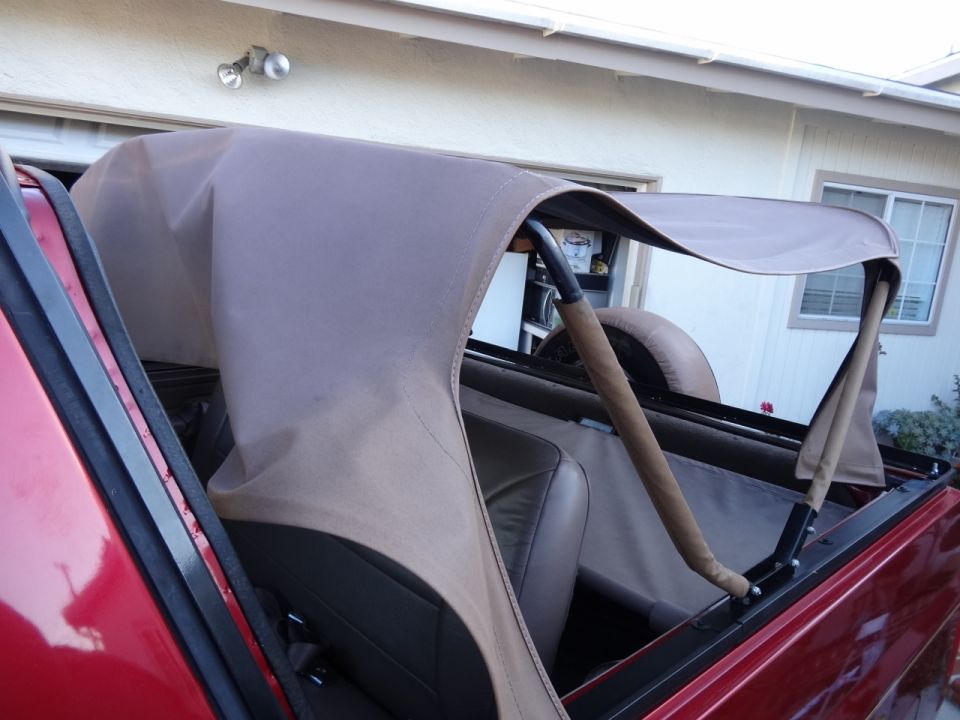 Tan soft top on a red convertible, partially deployed, showing interior and frame.