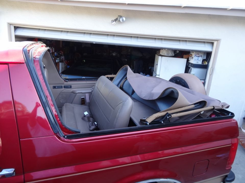 Red Bronco with hardtop off and tan soft top and bows laid in the rear cargo area