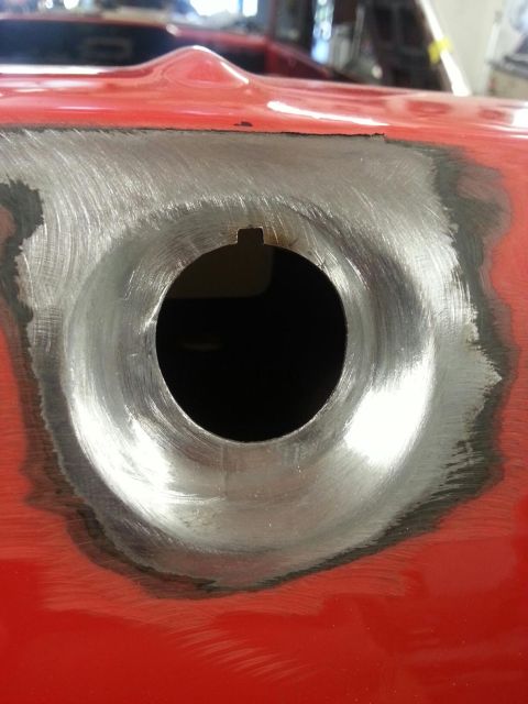 1964 Ford Fairlane - A close-up view of a circular metal area that has been sanded down to bare metal on a red car body. The sanded area surrounds a dark, circu…