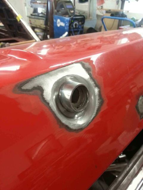 1964 Ford Fairlane - A close-up shot of a red car's fender where a circular metal piece, possibly a fuel filler neck, has been welded into place. The surroundin…