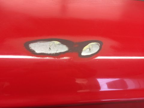 1964 Ford Fairlane - A close-up view of a red vehicle's body panel shows two areas that have been sanded and filled, likely for repair. The sanded areas reveal…