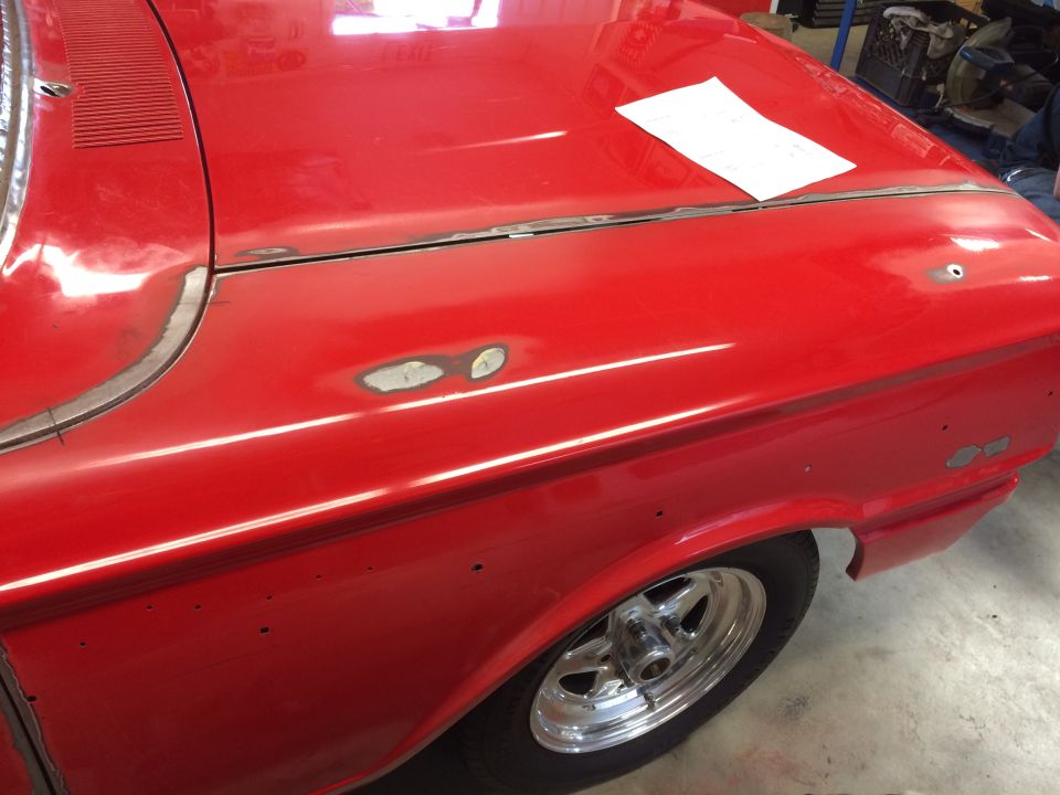 Red classic car fender and hood with bodywork, showing seams and primer.