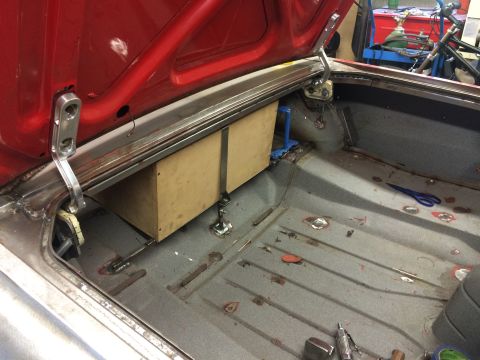 1964 Ford Fairlane - The open trunk of a red 1964 Ford Fairlane shows a custom wooden speaker box being installed. The trunk floor is gray and shows signs of re…