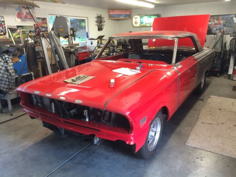 1964 Ford Fairlane - A bright red 1964 Ford Fairlane is parked in a garage, with its hood open, revealing the engine bay. The car is undergoing restoration, wit…
