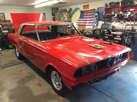 1964 Ford Fairlane - A red 1964 Ford Fairlane is parked in a garage with its hood open. The car is undergoing restoration, with the front grille and bumper remo…