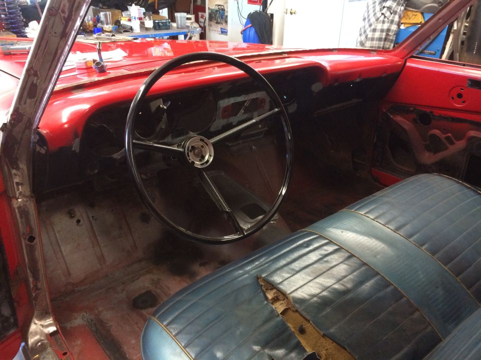 Interior of a red classic car with a black steering wheel and blue seat.