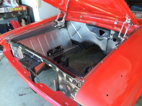 1964 Ford Fairlane - The engine bay of a red 1964 Ford Fairlane is shown with the hood open, revealing exposed metal components and the firewall.