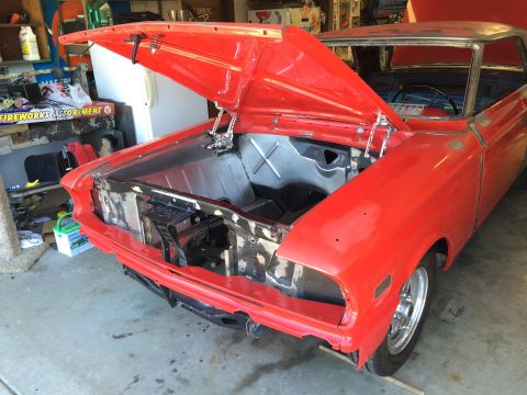 1964 Ford Fairlane - A red 1964 Ford Fairlane is in a garage with its hood open, revealing the engine bay. The car appears to be undergoing restoration or modif…