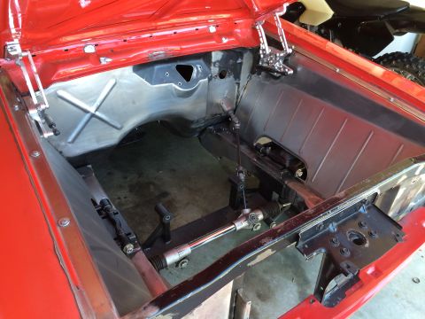 1964 Ford Fairlane - The engine bay of a red 1964 Ford Fairlane is shown, with the hood open and the engine removed. The firewall and inner fenders have been cl…