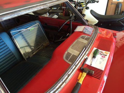 1964 Ford Fairlane - The interior of a red classic convertible is shown, with blue vinyl seats and a disassembled windshield frame. Tools and a small container…