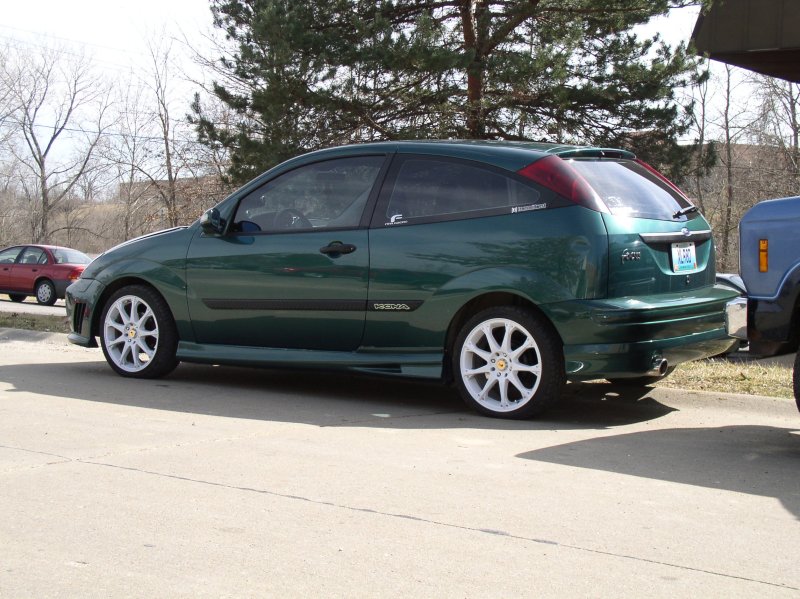 Green hatchback car with white wheels parked on asphalt, side view