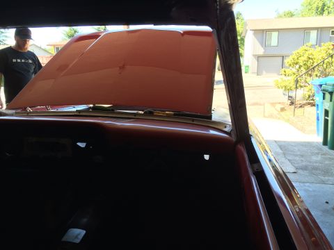 1964 Ford Fairlane - The interior of a classic red car with the hood open, showing the engine bay. A man in a black t-shirt and baseball cap is visible looking…