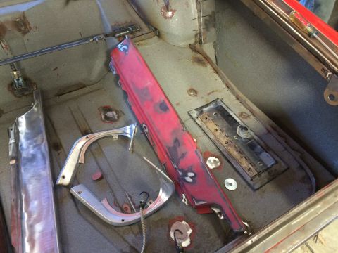1964 Ford Fairlane - The interior of a classic car undergoing restoration shows the floor pan with various metal parts, including a red-painted trim piece and a…