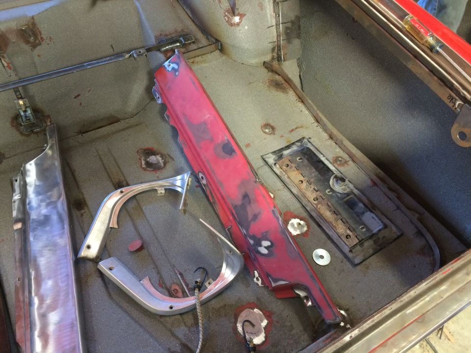 Interior of a classic car floor pan with restoration parts including red trim and polished metal.