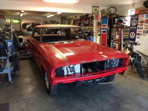 1964 Ford Fairlane - A bright red 1964 Ford Fairlane is parked in a garage, with its front end disassembled for repair or modification. Other vehicles and garag…