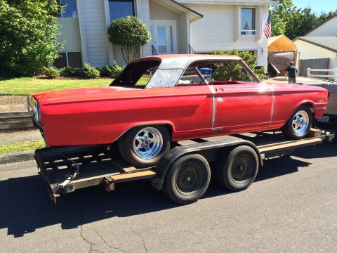 1964 Ford Fairlane - A bright red 1964 Ford Fairlane coupe is loaded onto a trailer for transport. The car appears to be undergoing restoration, with some body…