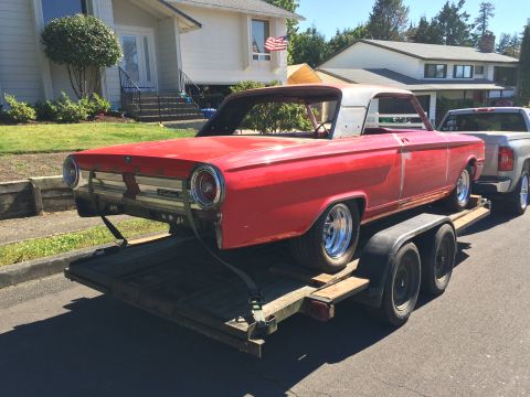1964 Ford Fairlane - A red 1964 Ford Fairlane is being transported on a flatbed trailer, towed by a silver pickup truck. The classic car is missing its roof and…