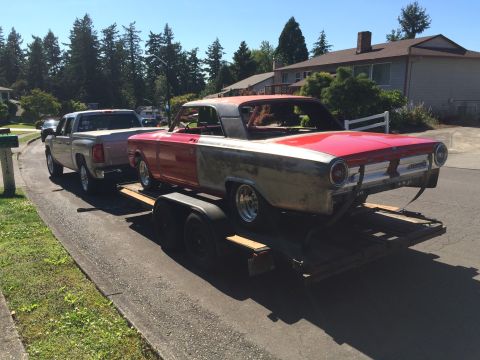 1964 Ford Fairlane - A red and silver classic car, likely a 1964 Ford Fairlane, is being transported on a trailer towed by a silver pickup truck. The car appear…