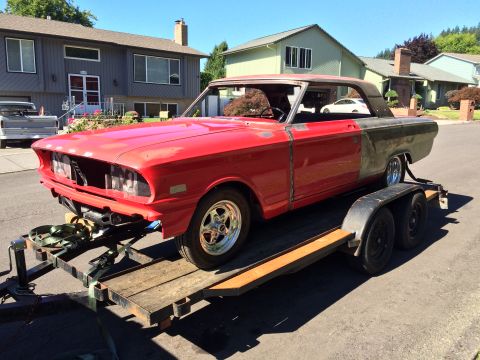 1964 Ford Fairlane - A red 1964 Ford Fairlane coupe is being transported on a trailer. The car is missing its front grille and headlights, and the rear quarter…