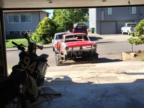 1964 Ford Fairlane - A red 1964 Ford Fairlane is loaded onto a trailer, being towed by a silver pickup truck. A motorcycle with the number 94 is parked in the f…