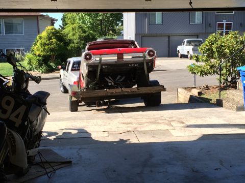 1964 Ford Fairlane - A red classic car is being towed on a trailer by a silver pickup truck. A motorcycle is parked in the foreground, partially obscuring the v…